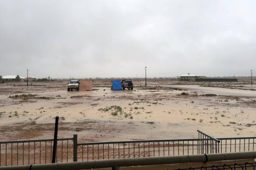 Two four-wheel-drives with tents set up in a flat, rain-soaked paddock.