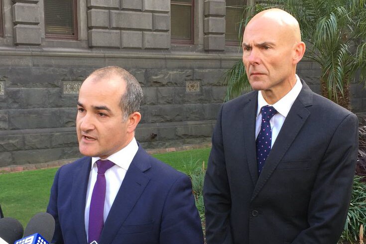 James Merlino speaking at a microphone at the doorstop with Andrew Crisp behind him.