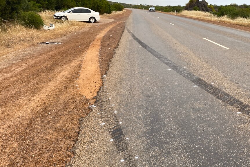 white car at the side of a sealed road with tyre marks on the road showing the path of the vehicle