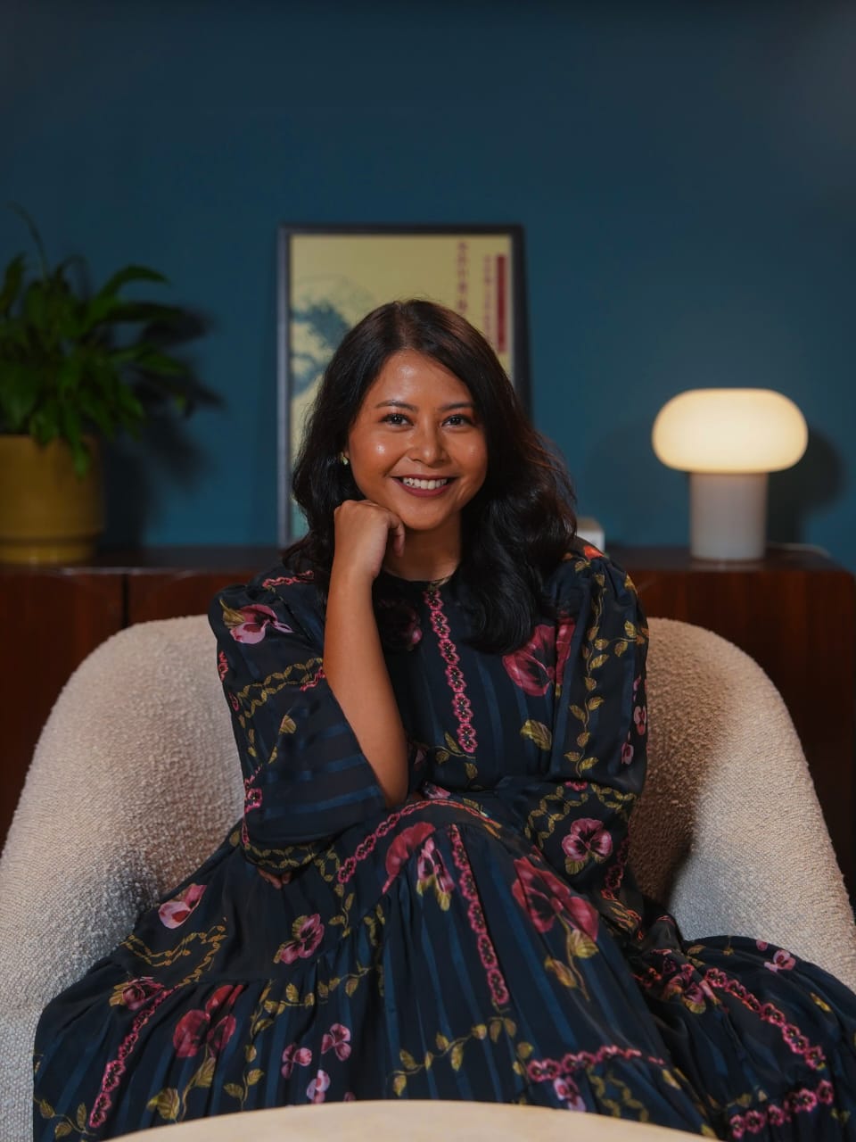Una mujer de pelo largo con un vestido sentada en un sofá con una mano debajo de la barbilla.