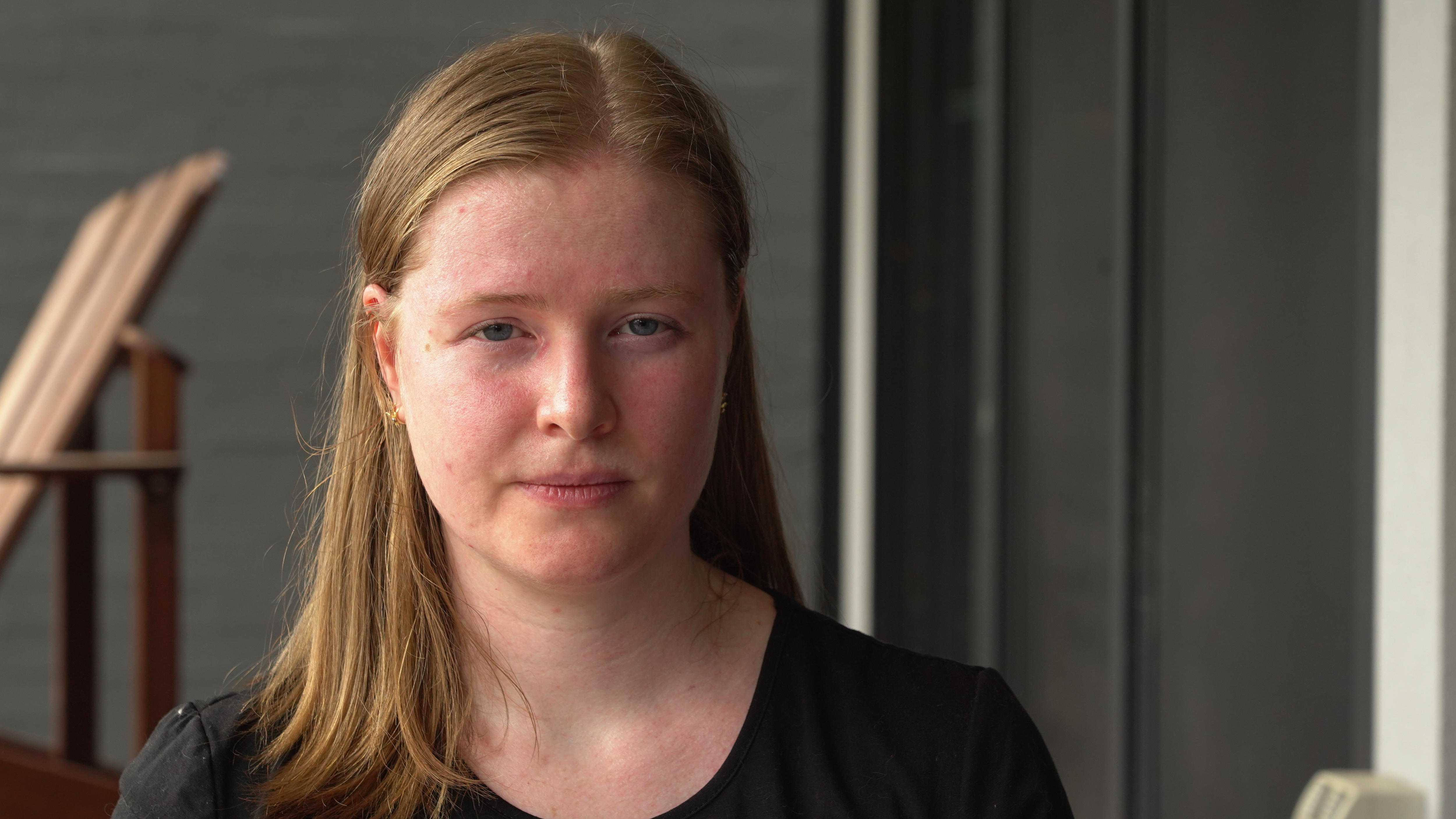 A woman with a straight face looks at the camera.