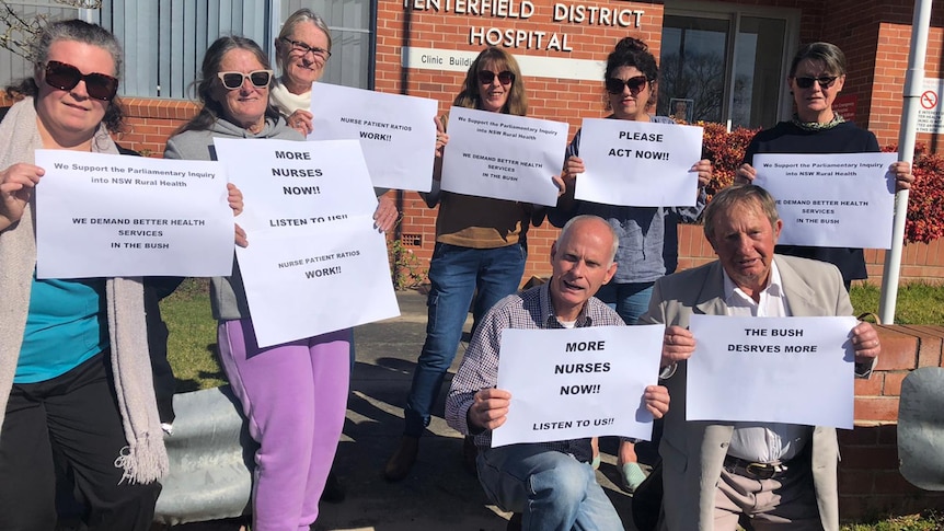 Eight people holding signs outside a brick building.