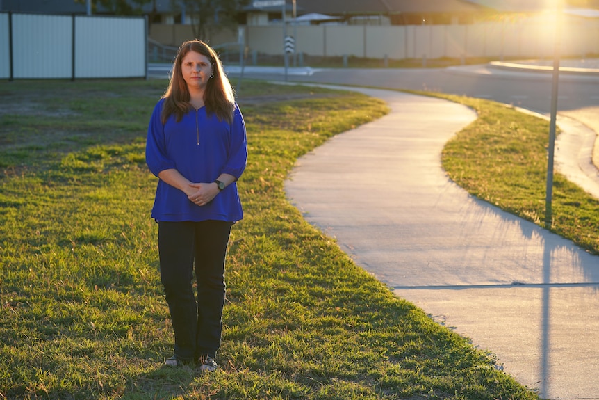 A silhouette of a woman wearing pants and a top standing on a pathway of a suburban street at dusk