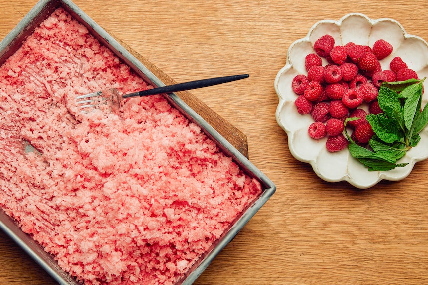 A baking tray filled with watermelon and rose granita, with a fork for scraping. An easy summer dessert.