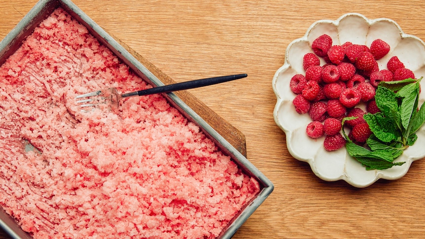 A baking tray filled with watermelon and rose granita, with a fork for scraping. An easy summer dessert.