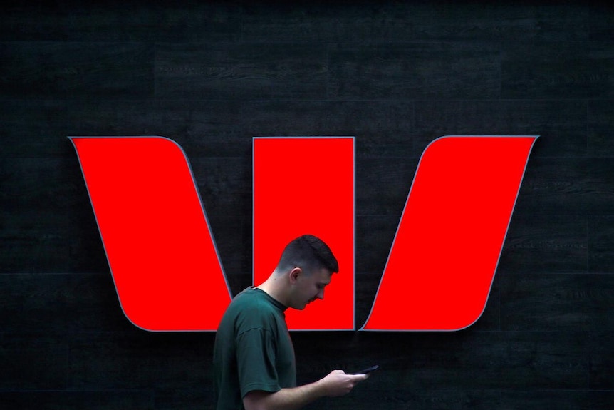 A pedestrian looks at his phone as he walks past a Westpac logo