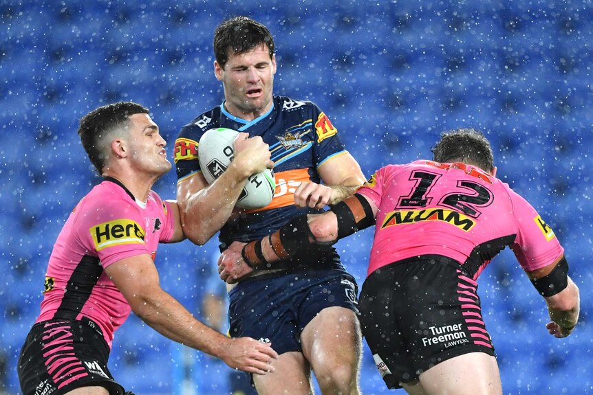 Gold Coast Titans' Anthony Don is hit hard in a tackle by Penrith Panthers. It is raining.