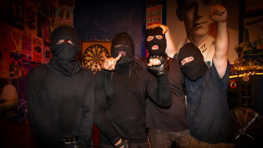 Band members wearing all black with faces covered by masks. 