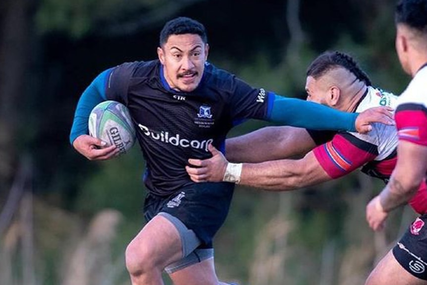 A pacific islander rugby player fending off a tackle while running with the ball 