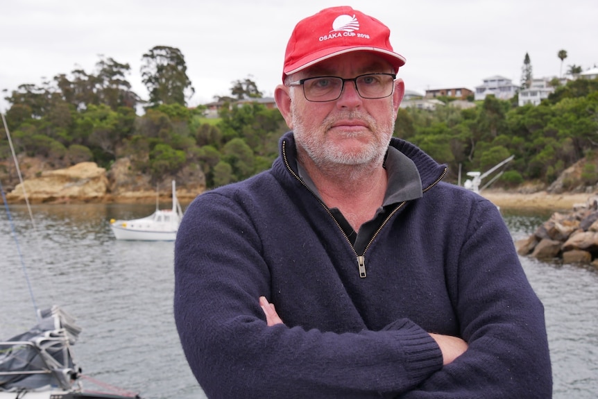 A bearded man with a red cap stands on a jetty