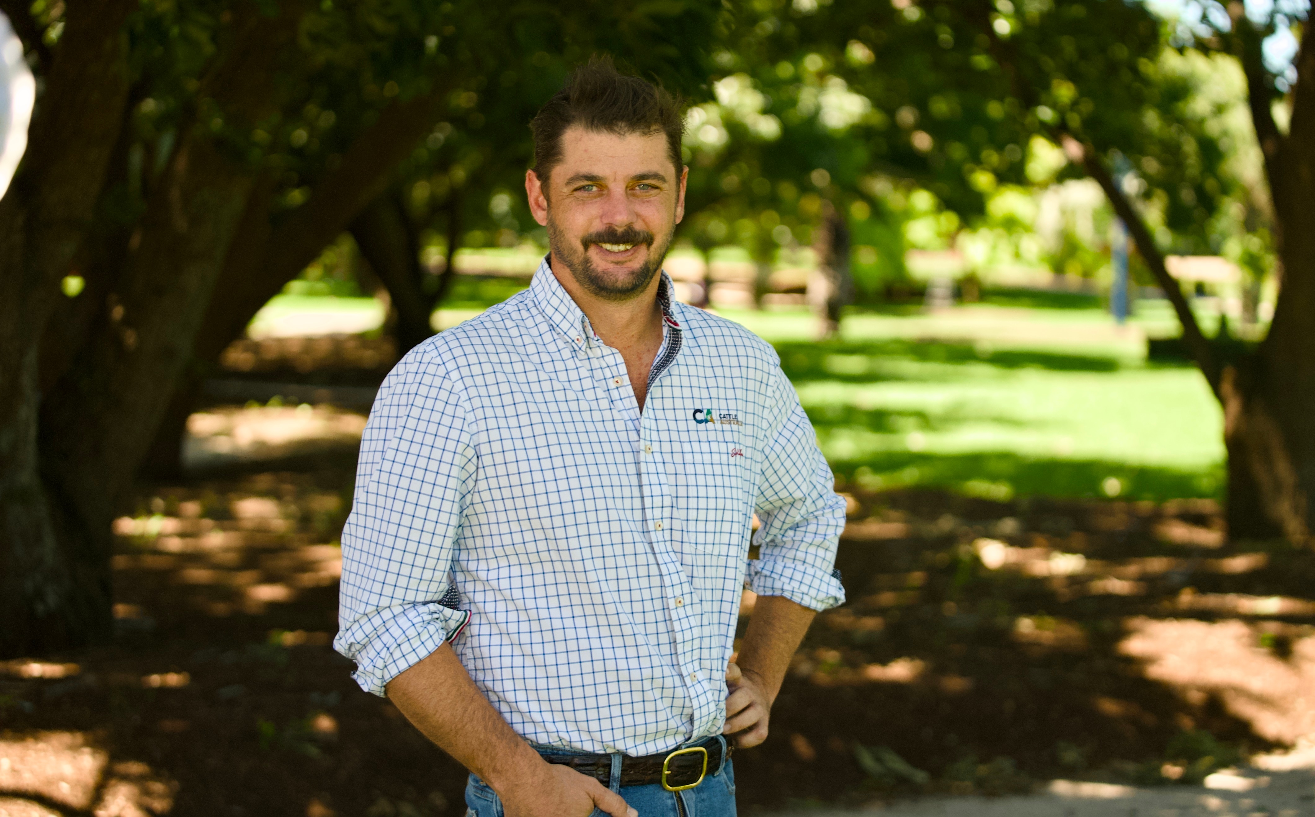 Un hombre se encuentra en un parque sombreado y sonríe a la cámara.