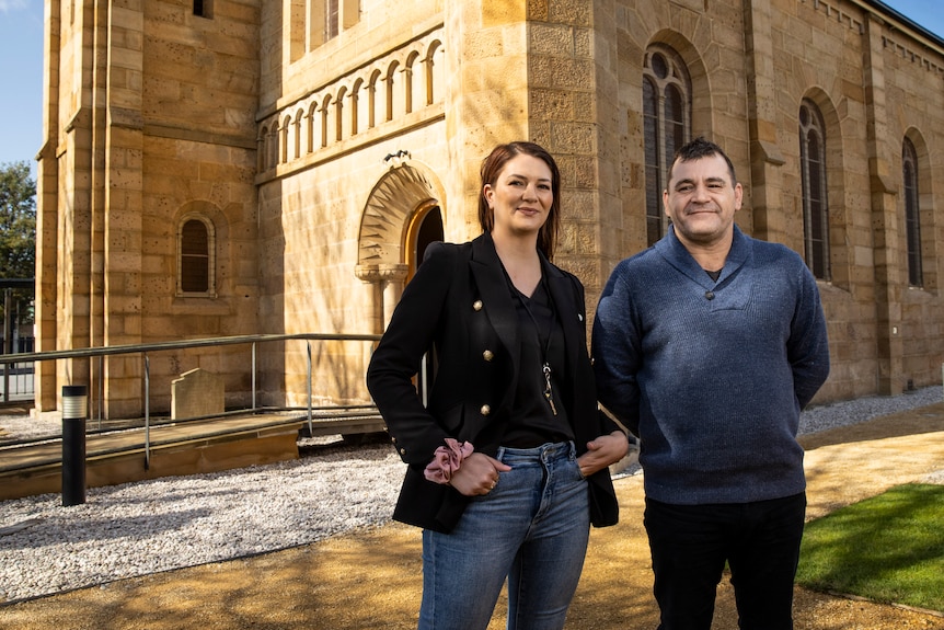 A woman and a man stand in front of a brick building.