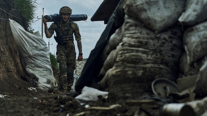 A Ukrainian soldier carries supplies in a trench at the frontline.