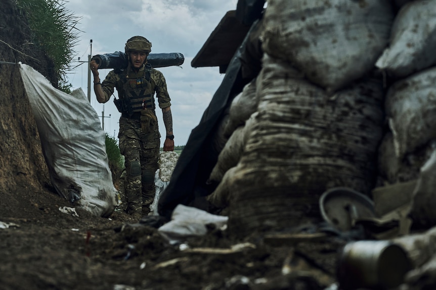A Ukrainian soldier carries supplies in a trench at the frontline.