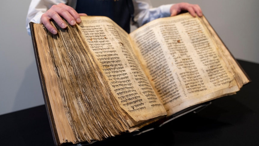 A man holds open a large old book.