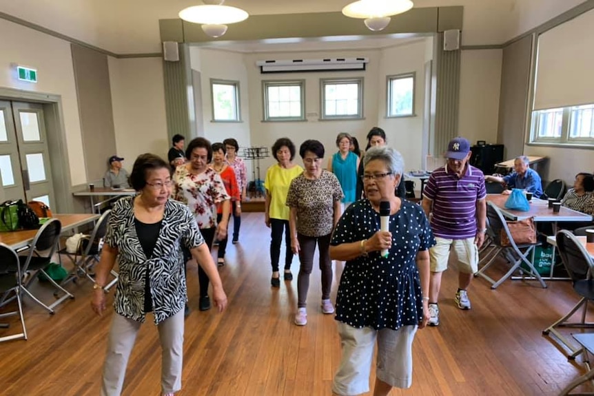 A group of elderly people dancing an one woman holding a microphone.