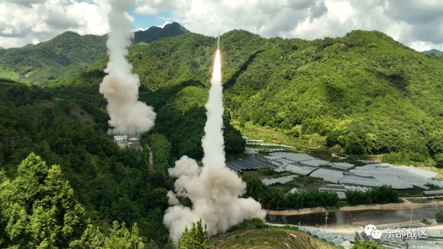 Chinese missiles leave the ground in a cloud of smoke from between lush mountians.