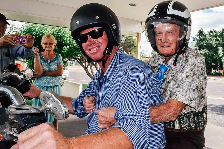 Two men in helmets sit on a motorbike