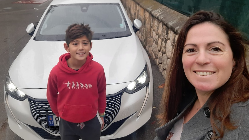 A brunette woman and a young boy before a new white car