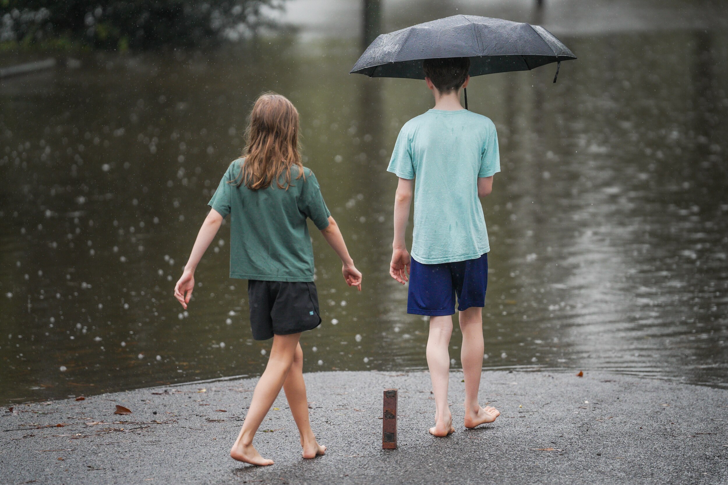 Two children stand in front of a flooded street staring at the water.