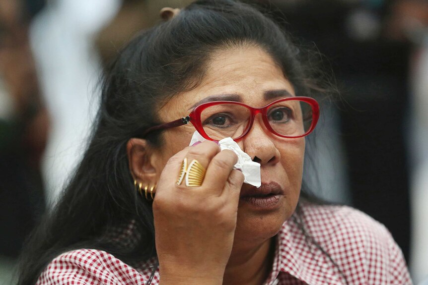 A Thai woman with red rimmed glasses wipes her eyes with a tissue after the party she supports was dissolved by a Thai court.