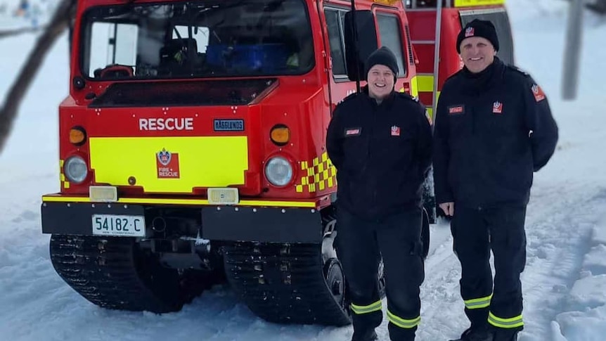 Two firefighters standing next to a snow fire truck in the snow.