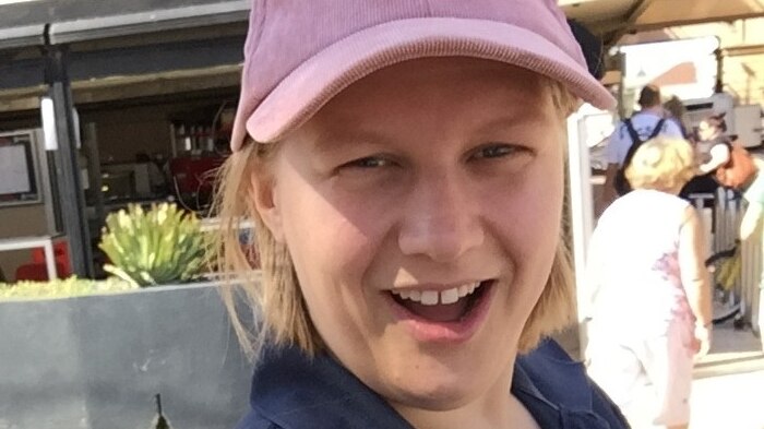 A blonde woman wearing a pink cap smiling at the camera