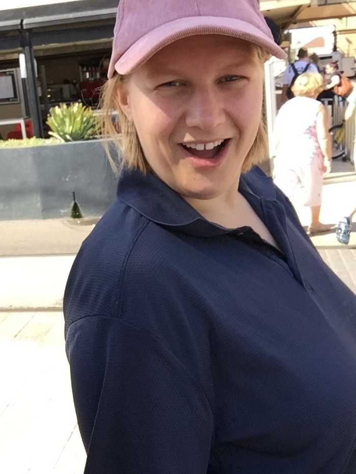 A blonde woman wearing a pink cap smiling at the camera