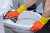 A woman cleaning a toilet bowl in a bathroom.