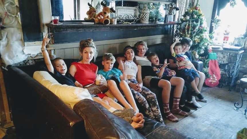 Six kids and two teenagers squeeze onto a couch together near a Christmas tree.