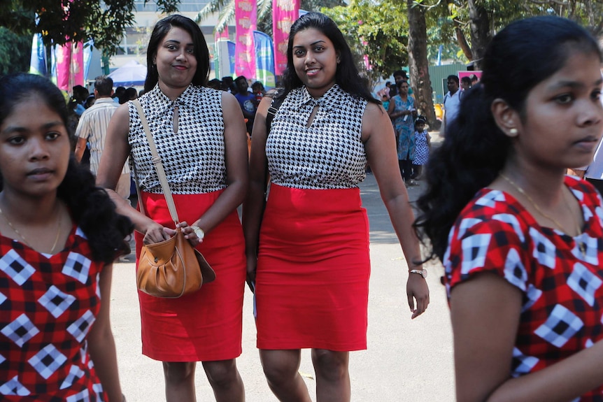 Two young women who are twins wearing a houndstooth sleeveless top and orange pencil skirt.