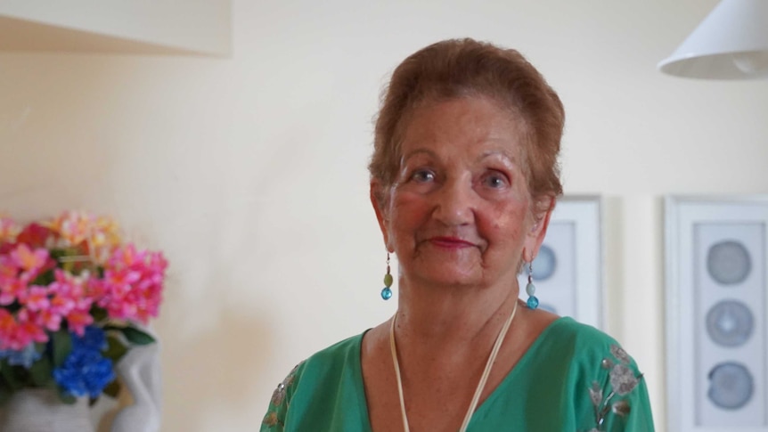 A woman with blue dangly earrings and a green top looks at the camera