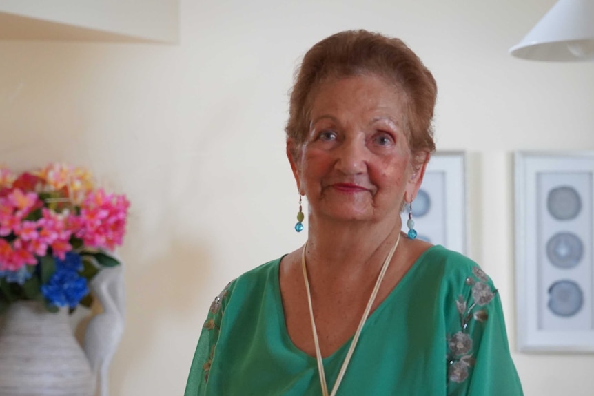 A woman with blue dangly earrings and a green top looks at the camera