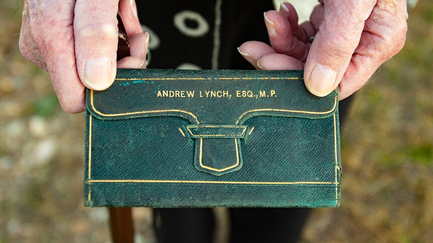 An elderly person's hands holding a green wallet.