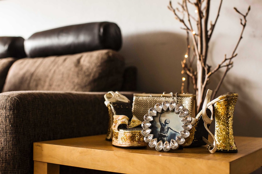 Glittery high heels and a picture of a dancer sit on coffee table beside brown couch.