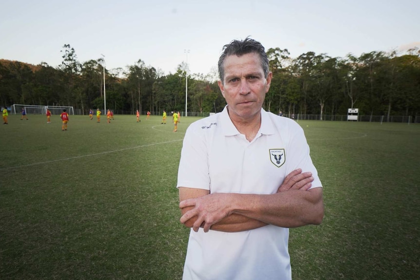 Man in a white shirt in front of community soccer players.