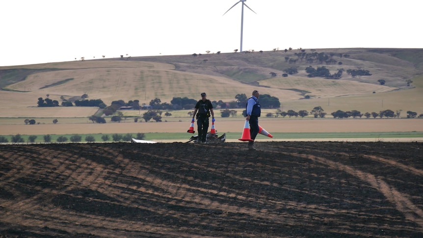 A blackened field following a fire caused by a deadly light plane crash, with police walking and positioning traffic cones.
