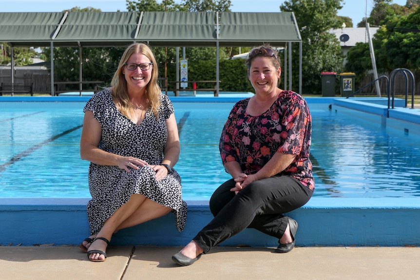 two women sitting next to a pool