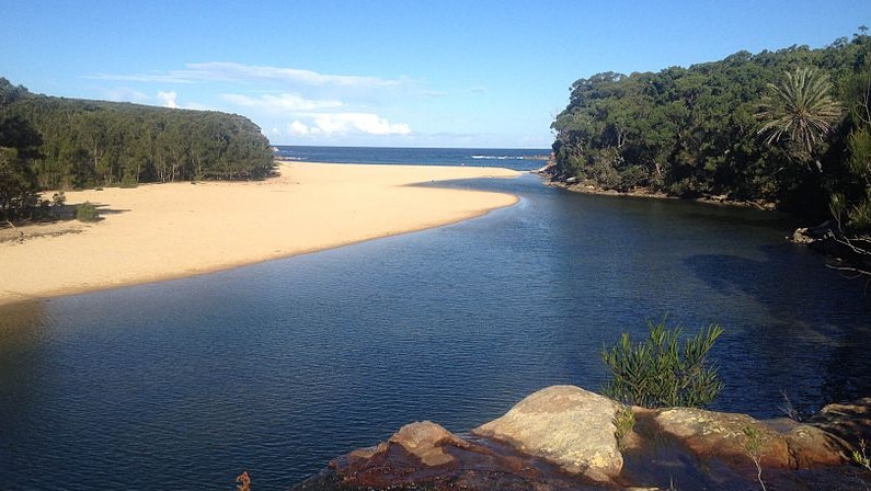 Wattamolla lagoon, featuring a waterfall and a beach in the background.