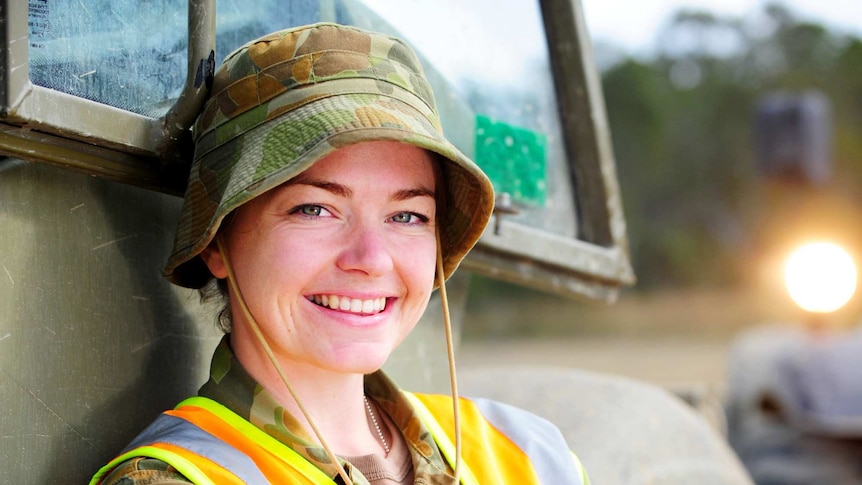 Captain Angela Stokes wears an army uniform with a high-visibility vest while standing against a truck