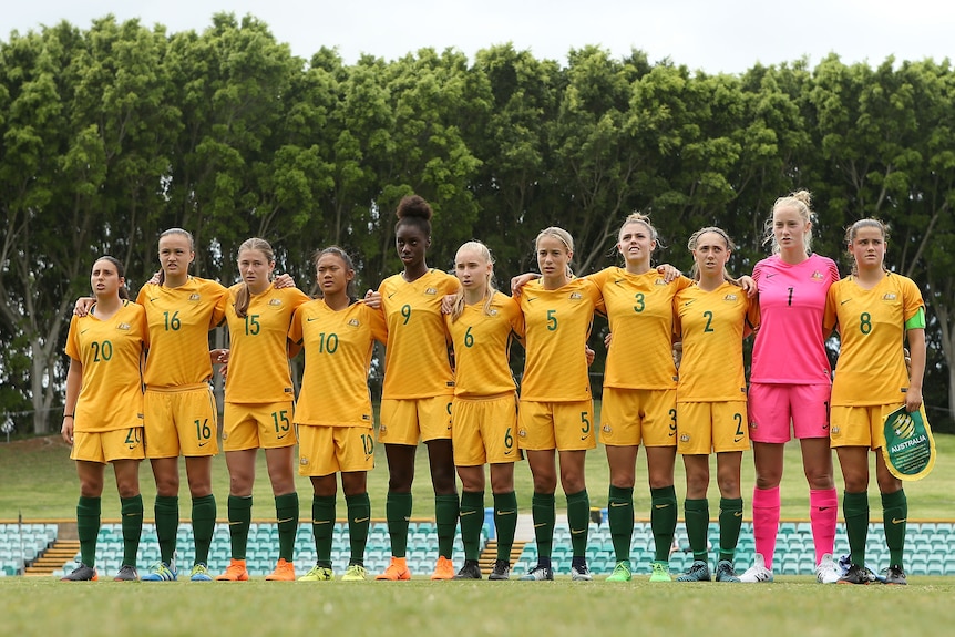 Australia soccer players wearing yellow uniforms link arms as they line up before a match