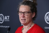 A woman wearing glasses with hair tied up speaks at a press conference