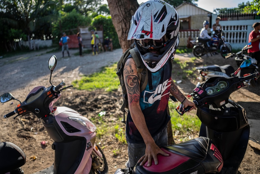 A person in a motorcycle helmet stands over an e-scooter. He has a detailed tattoo of woman on shoulder