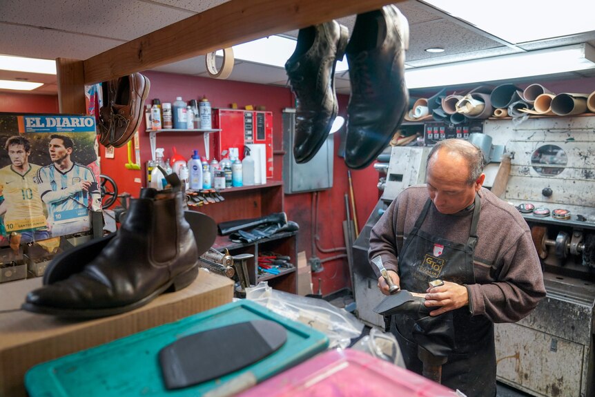 A man repairing a shoe behind a counter with boots on a bench in front of him