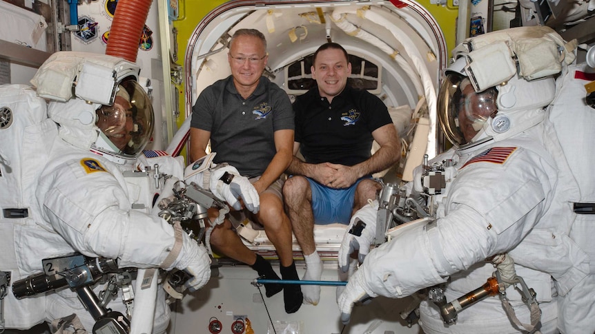 Two astronauts in space suits flank two astronauts out of their suits.