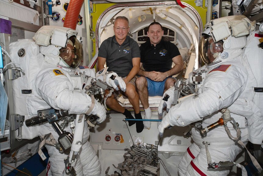 Two astronauts in space suits flank two astronauts out of their suits.