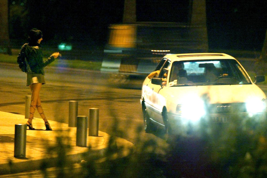 A car stops next to a prostitute standing on a street corner on the French Riviera.