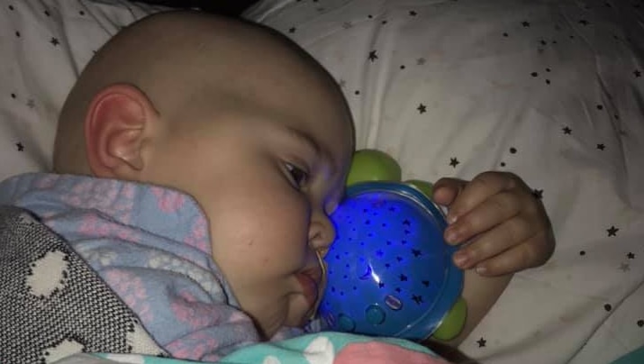 A baby snuggles in bed with her blue turtle-shaped night-light.