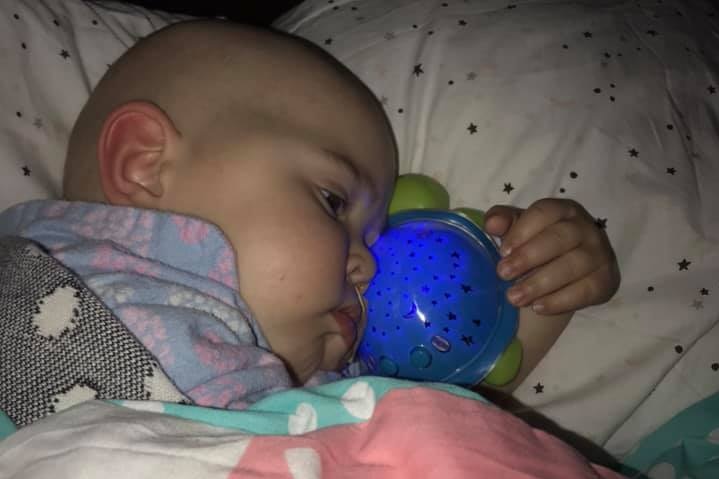 A baby snuggles in bed with her blue turtle-shaped night-light.