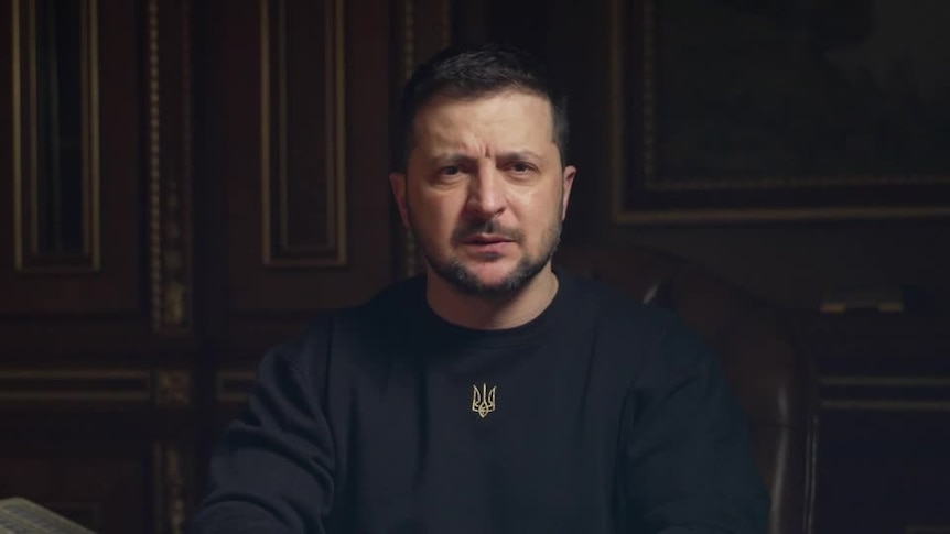 Close up of Ukrainian President speaking to camera wearing black shirt with Ukraine's trident symbol.